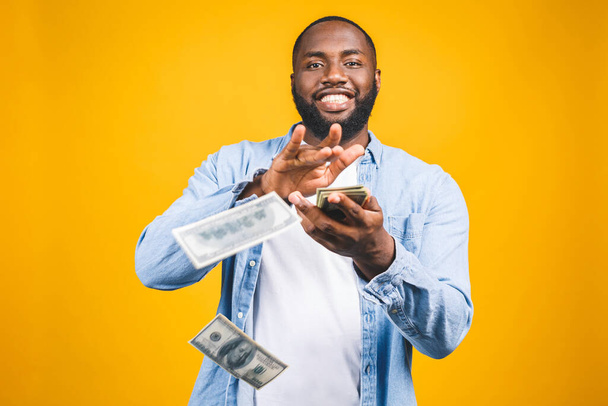 Portrait of a happy young afro american man throwing out money banknotes isolated over yellow background. - Fotoğraf, Görsel