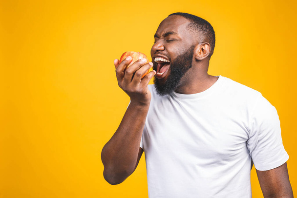 Un homme afro-américain en bonne santé tenant une pomme isolée sur fond jaune.  - Photo, image