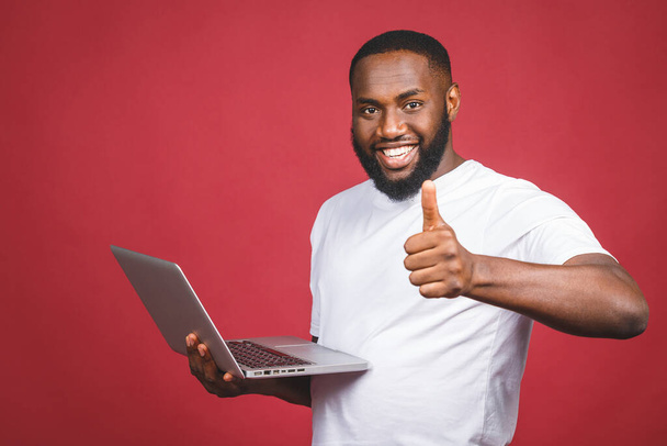Innoissaan onnellinen afro amerikkalainen mies tietokoneen näytön ja juhlii voittaa eristetty yli punainen tausta. Peukut pystyyn.. - Valokuva, kuva