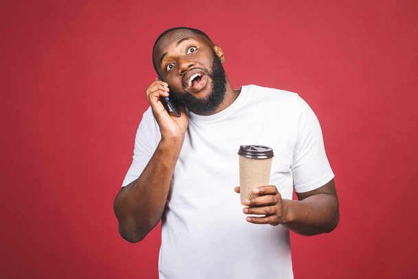 Retrato de um belo homem afro-americano surpreso com telefone celular e levar copo de café. Isolado sobre fundo vermelho. - Foto, Imagem