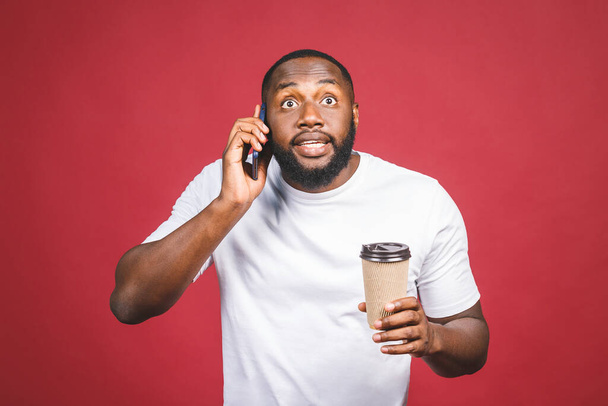 Retrato de um belo homem afro-americano surpreso com telefone celular e levar copo de café. Isolado sobre fundo vermelho. - Foto, Imagem