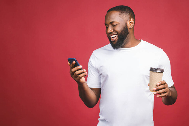 Guapo afroamericano con teléfono móvil y llevar taza de café. Aislado sobre fondo rojo. - Foto, Imagen