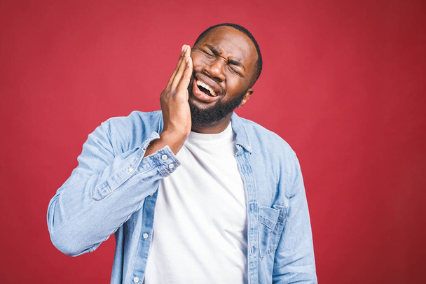 Young black man isolated on red background with mouth open, touching his face with expression of horrible suffer from health problem and aching tooth. - Photo, image