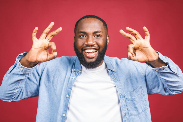 Happy young African-American man isolated against red background. Ok sign. - Fotografie, Obrázek