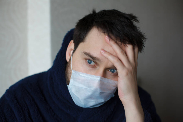 Overhelmde man in medicijnmasker met zijn hand op een voorhoofd. Hoe kalm te blijven tijdens een coronaviruspandemie - Foto, afbeelding