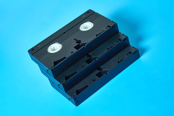 Heap of black old plastic vhs video cassettes lies on blue desk. Concept of 90s. Close-up - 写真・画像