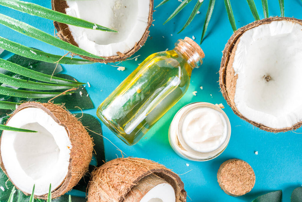 Aceite de coco en frasco de vidrio con hojas tropicales y coco fresco. Concepto de aceites mct orgánicos. turquesa, fondo aguamarina - Foto, imagen