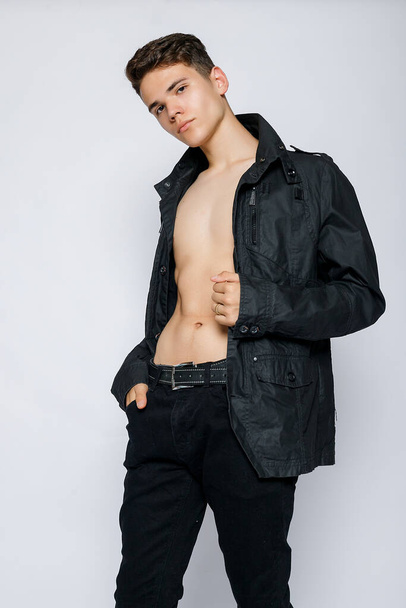 Young muscular man in a black jacket and jeans. young handsome man, leather jacked on naked torso, emotional posing, white background, modern guy, lifestyle people concept - Foto, Imagen