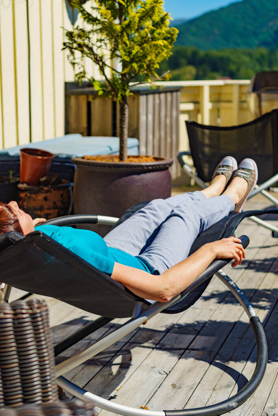 Relax in the sun. Adult woman relaxing resting in deck chair outdoor on veranda. Holiday cottage. - Photo, Image
