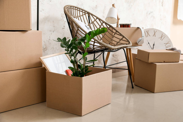 Χάρτινα κουτιά με αντικείμενα και πολυθρόνα σε νέο διαμέρισμα κατά την ημέρα κίνησης - Φωτογραφία, εικόνα