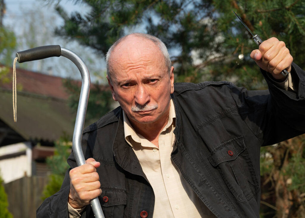 Yaşlı bir adam dışarıda baston ve bıçakla tehdit ediyor. - Fotoğraf, Görsel