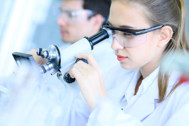 Nuori naistutkija, joka etsii mikroskoopilla laboratoriosta, suorittaa kokeen tai tutkimuksen. Terveydenhuollon teknologian, farmaseuttisen tutkimuksen ja kehityksen käsite. - Valokuva, kuva