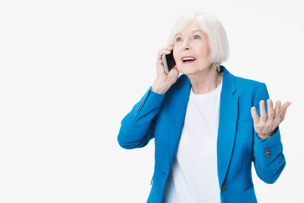 Positive senior woman smiling while talking on the phone and excited isolated over white background - Fotó, kép