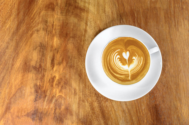 Ζεστός καφές latte σε λευκό κεραμικό κύπελλο και πιατάκι τοποθετείται σε ξύλινο τραπέζι με χώρο αντιγραφής (Top view) - Φωτογραφία, εικόνα