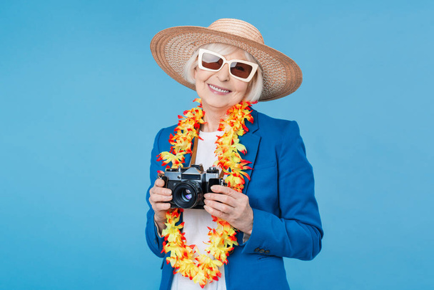 Senior woman traveler with retro photo camera isolated on blue background - Foto, afbeelding