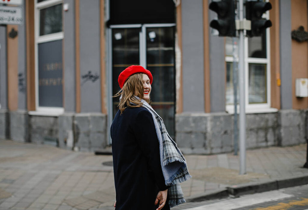 colorful blonde girl in a red hat, coat and scarf on a walk in the city smiling - Fotografie, Obrázek