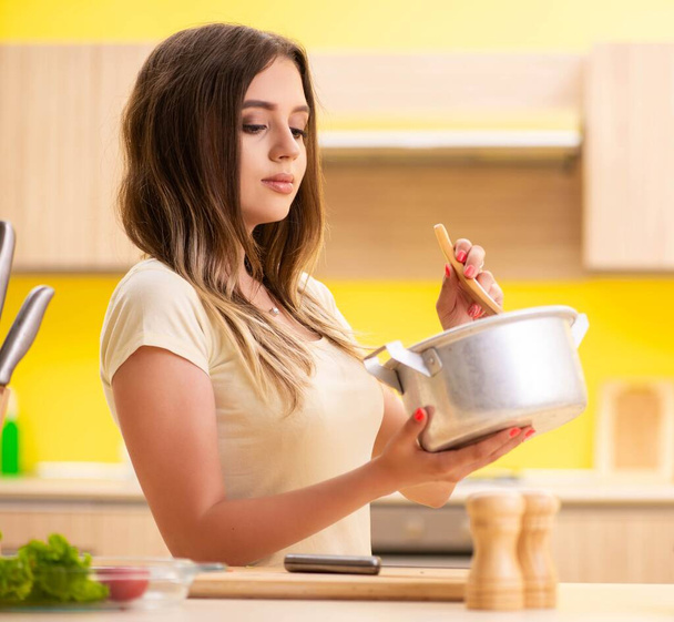 Молодая женщина готовит суп на кухне дома - Фото, изображение
