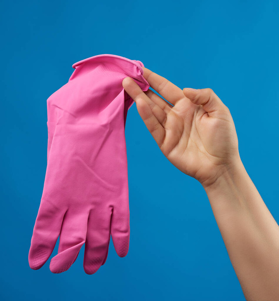 женская рука держит розовые резиновые перчатки для чистки, синий фон, защитная одежда для уборки дома
 - Фото, изображение