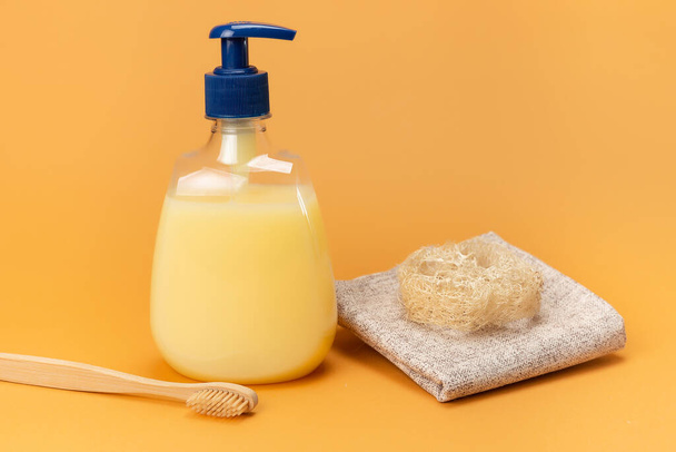 Egy üveg folyékony szappan sárga és bambusz fogkefe természetes anyagból készült szivaccsal bézs alapon. Tiszta kéz koncepció. Sampon, folyékony szappan, aromás fürdősó és egyéb WC. - Fotó, kép