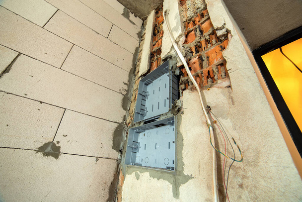 Kable elektryczne umieszczone na plastikowej skrzynce bezpieczników zamontowane na ścianie w pomieszczeniu w trakcie prac budowlanych. - Zdjęcie, obraz