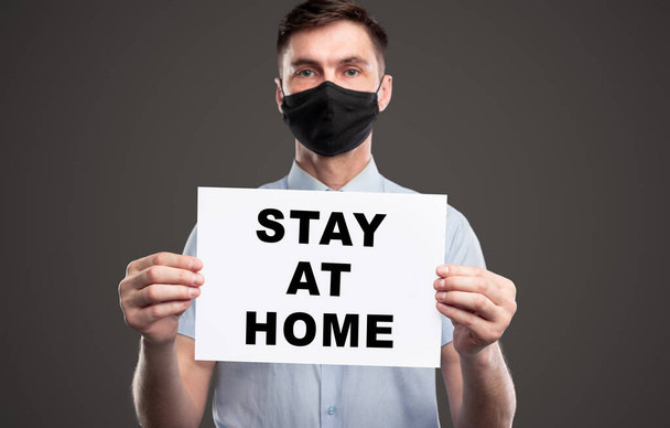 Man in protective mask holding paper with Stay At Home text - Fotoğraf, Görsel