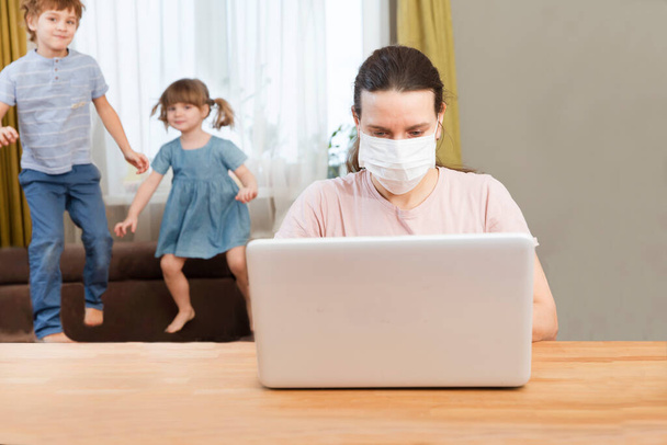 Home office. Working from home vs. Mom wearing medical face Works with two kids on the Internet on a laptop at home. quarantine. Corona Virus. - Fotografie, Obrázek