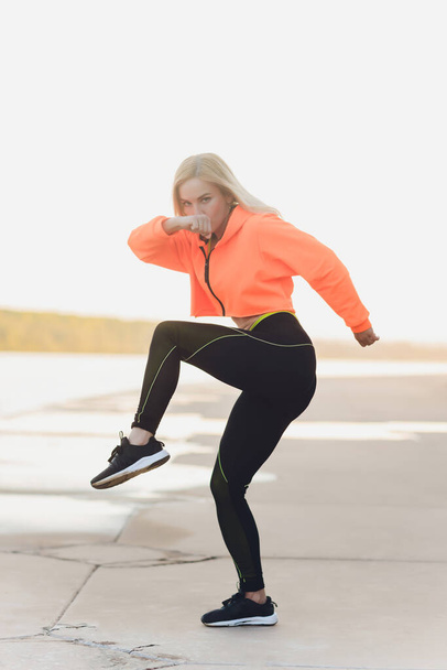Healthy woman training on seaside promenade. Young attractive woman in sportswear does stretching before exercise on the beach at sunrise. Warm up. - Φωτογραφία, εικόνα