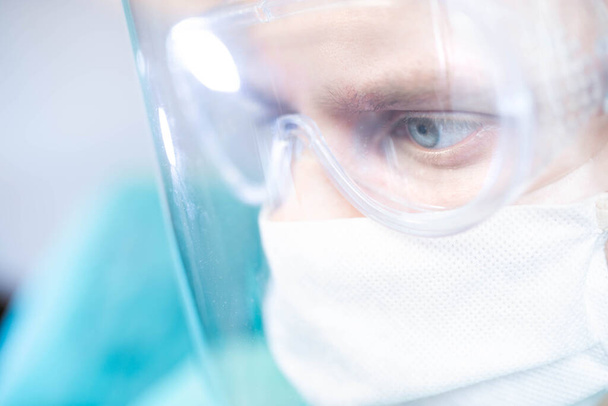 surgeon with glasses and a protective shield and mask. Young specialist works in the operating room - Photo, image