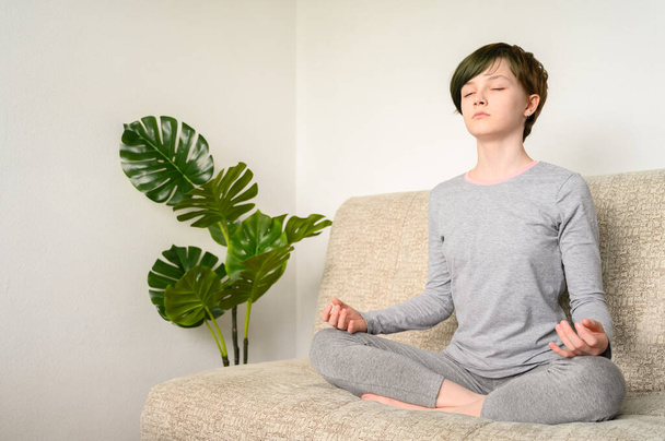 Adolescente meditar sentado em posição de lótus no sofá. Yoga em casa
. - Foto, Imagem