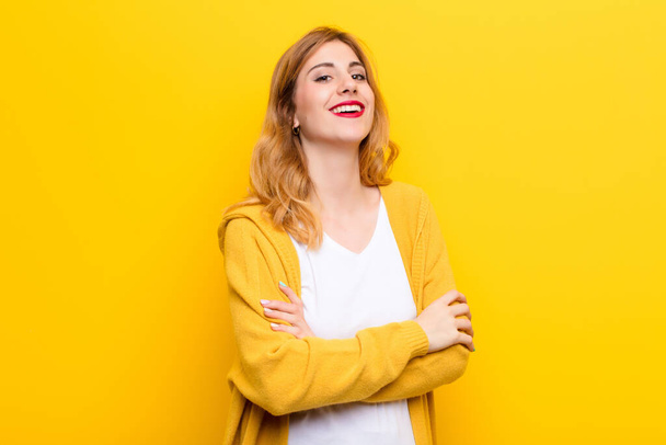 fiatal csinos szőke nő nevetve boldogan karok keresztbe, egy nyugodt, pozitív és elégedett póz ellen sárga fal - Fotó, kép