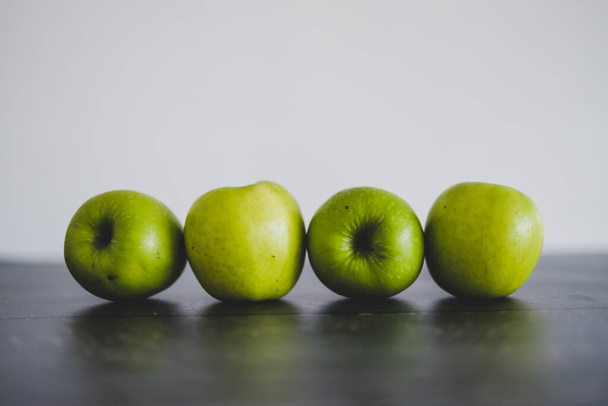 healthy plant-based food ingredients concept, green apples lined up on wooden table shot from eye-level perspective - Foto, Imagem