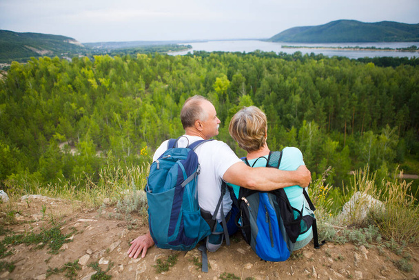 elderly couple with backpacks sits on the mountain. Senior couple walking in nature. travel tourism concept. Social Distancing. end of a quarantine. Staycations, hyper-local travel,  family outing, getaway, natural environ - Photo, Image