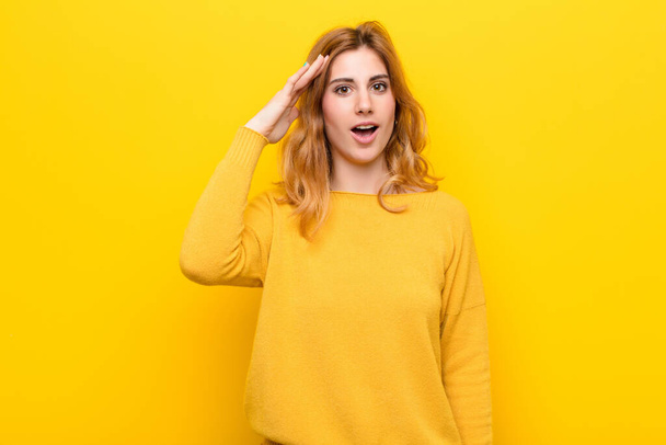 young pretty blonde woman looking happy, astonished and surprised, smiling and realizing amazing and incredible good news against yellow wall - 写真・画像