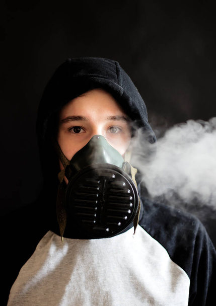 Teenager in a gas mask on a black background - Φωτογραφία, εικόνα