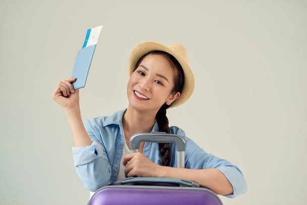 Retrato de una joven feliz sosteniendo boletos de viaje y pasaporte aislado sobre fondo claro
 - Foto, Imagen