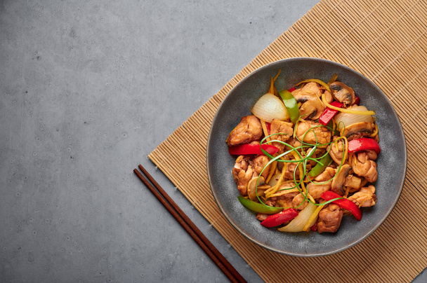 Thai Ginger Chicken or Gai Pad King in gray matte bowl on concrete backdrop. Gai Pad King is Thailand cuisine dish with chicken meat, ginger strips, onion, capsicum and sauces. Thai Food. Copy space - Photo, Image