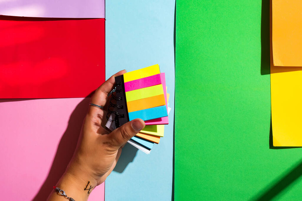Kleurrijke plakkerige notities in een vrouw hand op kleur papier achtergrond - Foto, afbeelding