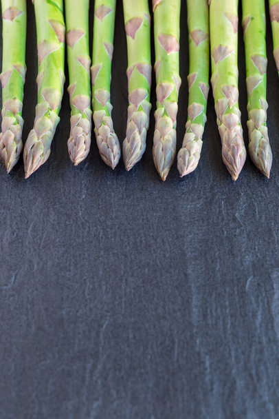 Bunch of fresh green asparagus on a dark slate background, vertical, copy space - Фото, изображение