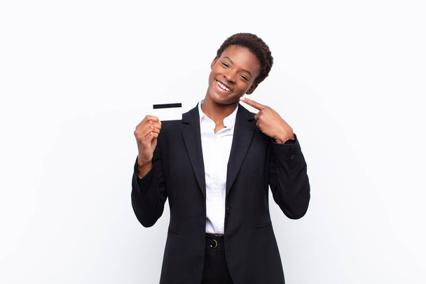 молодая красивая черная женщина уверенно указывая на свою широкую улыбку, позитивное, расслабленное, удовлетворенное отношение держа кредитную карту - Фото, изображение
