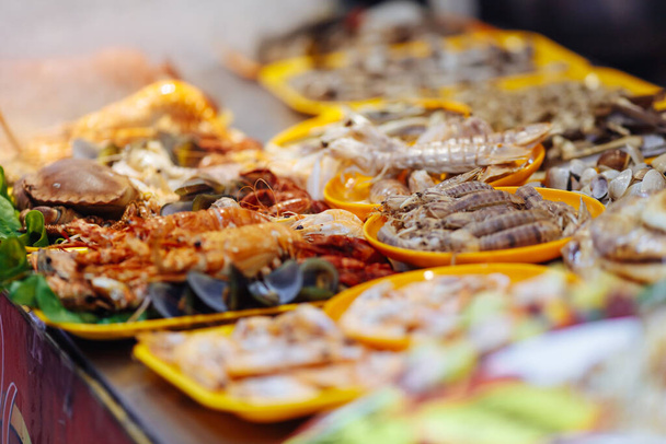 Variety of fresh seafood on plastic plates on weekend night market in exotic country. Delicious colorful asian meal for tourists. Blur background - Photo, Image