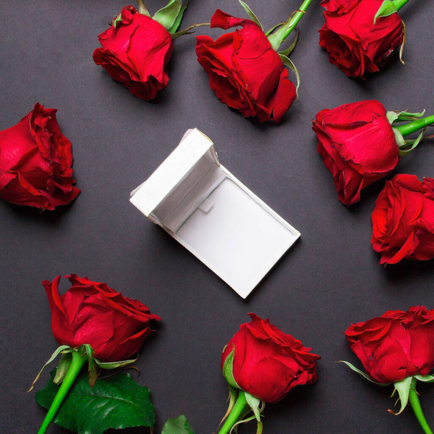 Rose rosse e scatola regalo aperta bianca su sfondo di carta di colore nero, foto quadrata
. - Foto, immagini