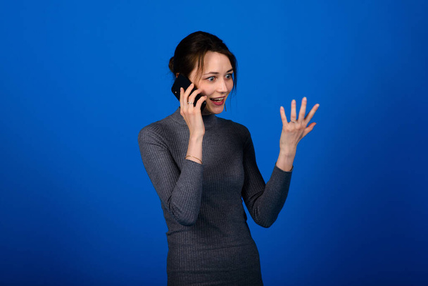 Image of a happy surprised shocked young pretty woman posing isolated over blue wall background using mobile phone. - Foto, imagen