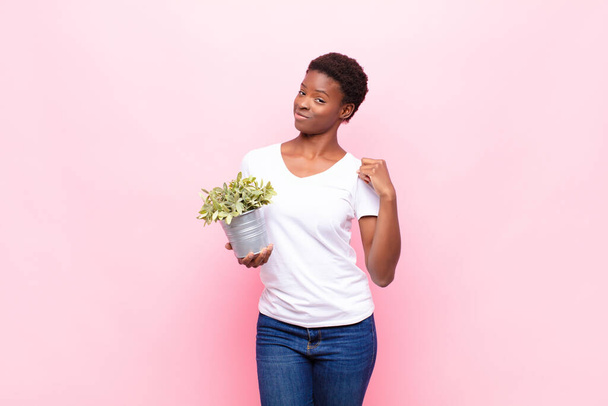 young pretty black womanlooking arrogant, successful, positive and proud, pointing to self holding a plant - Valokuva, kuva