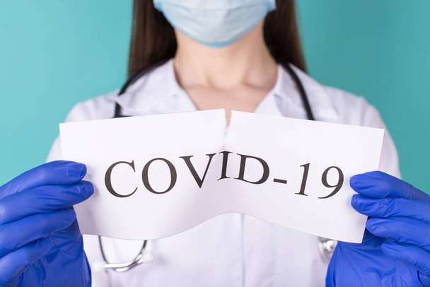 New coronavirus novel ncov overcome concept. Close-up cropped photo of professional doctor in white coat gloves tearing COVID-19 paper apart isolated on teal background - Photo, Image