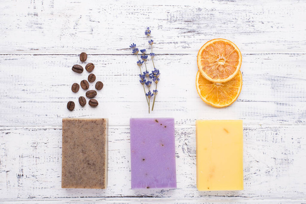 Top above overhead view photo of handmade organic soap bars with coffee beans lavender and dried orange slices isolated on white wooden background - Zdjęcie, obraz