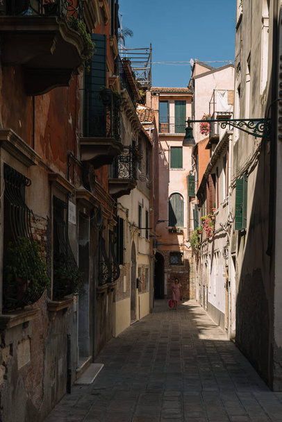 Venice, Italy - August 13, 2016: One woman is walking along the narrow and bright street of sunny Venice, Italy. - 写真・画像