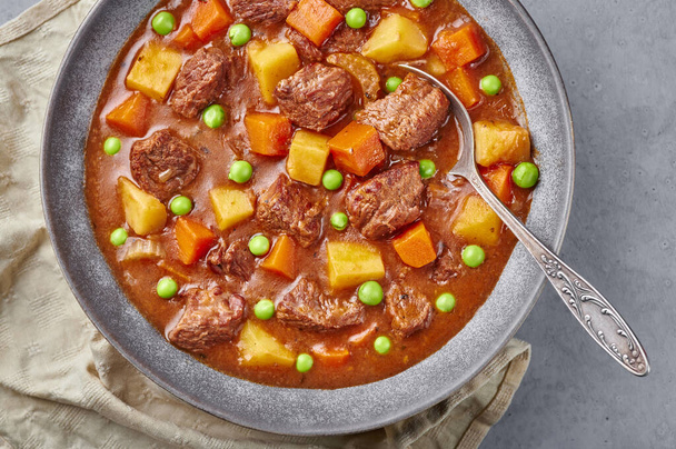 Irish Beef Stew in matt gray bowl on concrete background. Stew with beef or lamb meat with potatoes, carrots, peas and herbs. Traditional american and european food. Dinner mear - Photo, Image
