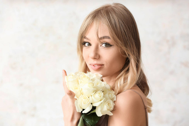 Gyönyörű fiatal nő csokor rózsa világos háttér - Fotó, kép