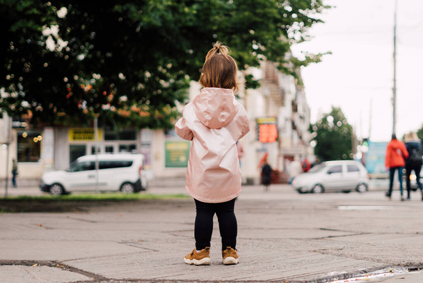 Portrait of child girl in pink raincoat outdoors. Lifestyle authentic portrait - Foto, immagini