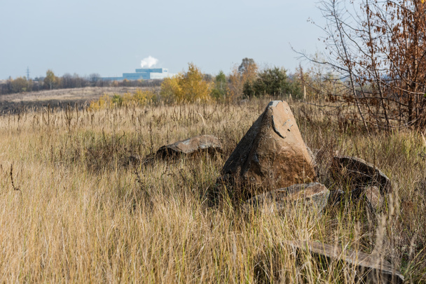 enfoque selectivo de rocas en el campo cerca de la fábrica y árboles verdes contra el cielo
  - Foto, imagen